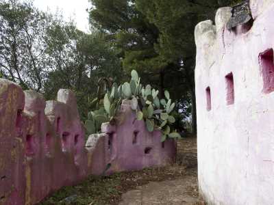 Varchiamo la soglia, venendo "accolti" da un vialetto costeggiato da muri rosa singolari: hanno una forma irregolare, sono contraddistinti da feritoie e a fatica resistono all'avanzare della vegetazione spontanea